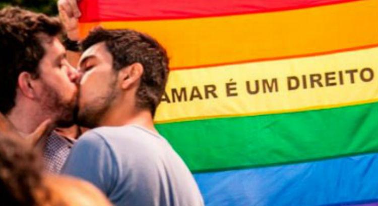 Casal gay se beija em frente a bandeira LGBT
