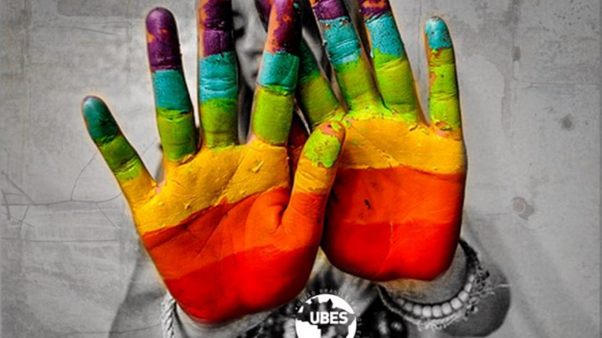 Menina escondendo o rosto com as palmas da mão pintadas pelo arco-Íris