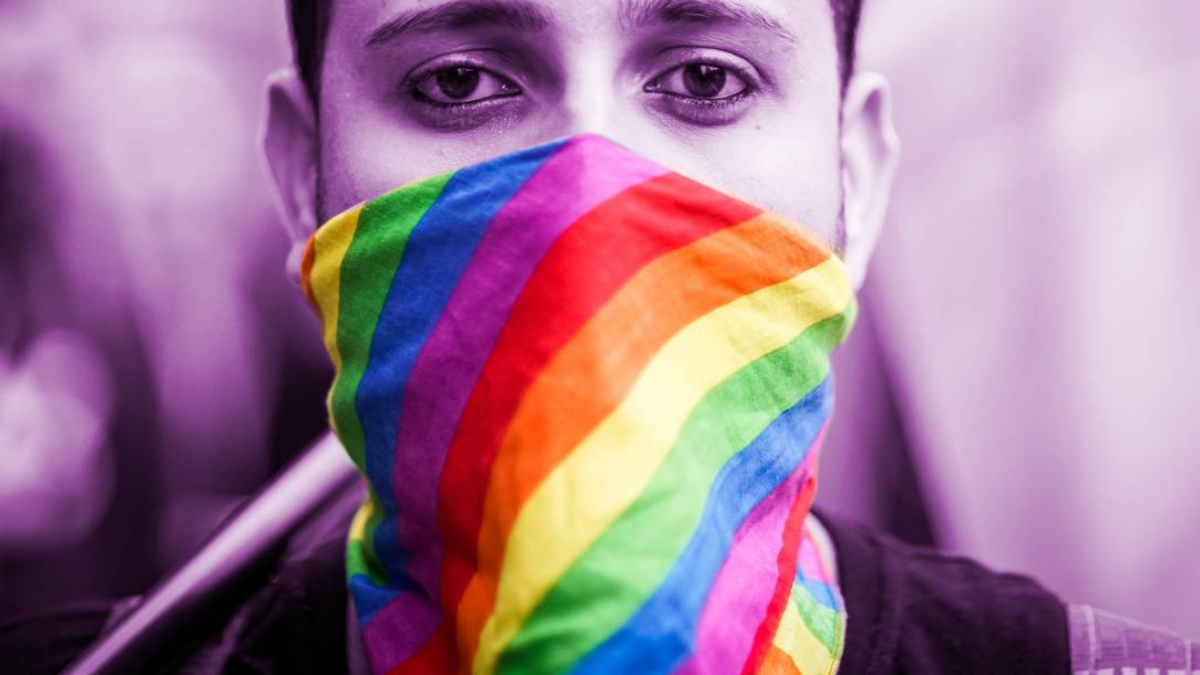 Menino com uma máscara na face representando as cores da bandeira LGBTQIA+