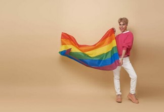Youth asian transgender LGBT with Rainbow flag isolated over nude color background. Man with a gay pride flag concept.