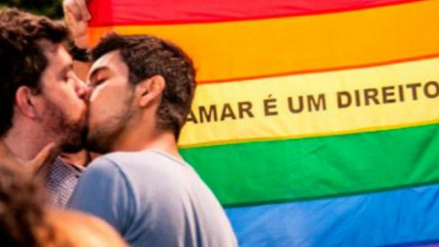 Casal gay se beija em frente a bandeira LGBT